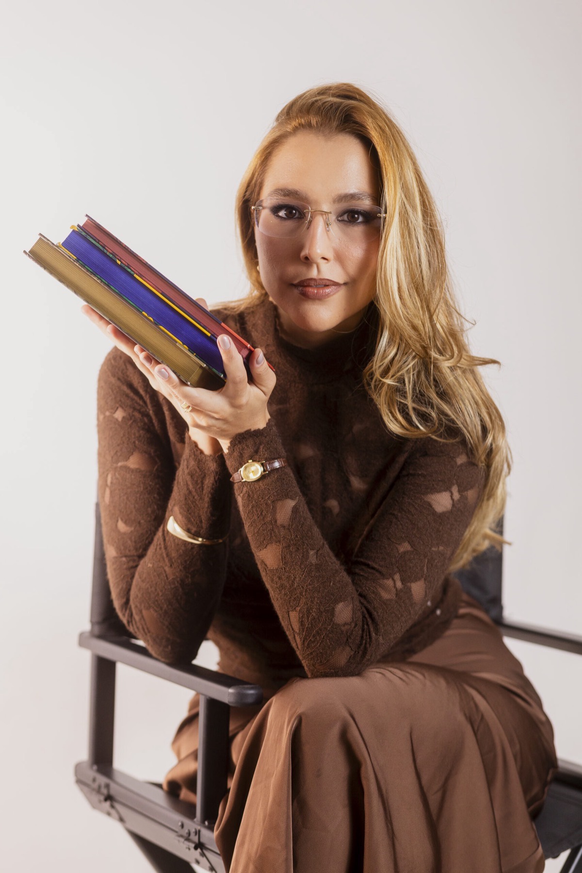 Ana Branco sentada, segurando livros, olhando para a câmera.